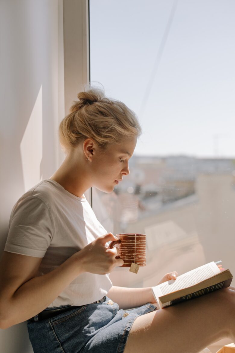 Bilden visar en person i fönster med en kaffekopp och en bok. En tätningslist har en viktig funktion för att energieffektivisera dina fönster.
